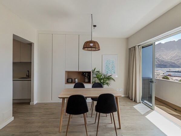A modern dining area with a wooden table, black chairs, a hanging light fixture, and a view of mountains through a large window. - Harbor & Sea View Agaete (Puerto de las Nieves)