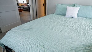 Een slaapkamer met een groot bed, een deur naar een andere kamer en een raam met gordijnen.