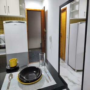 Una cucina compatta con mobili bianchi, un piano di lavoro nero e un piccolo angolo pranzo con una tazza gialla, un bicchiere e un piatto nero.