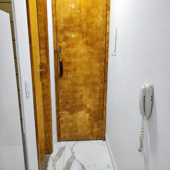 A narrow hallway with a wooden door, a white wall-mounted telephone, and a white door on the left. - Moderno Apartamento Centro de Curitiba (Curitiba)