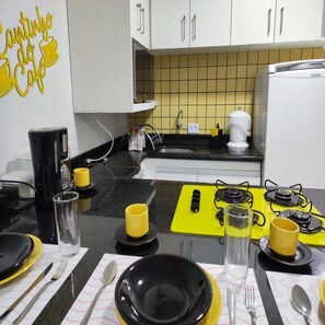 Una cucina con mobili bianchi, uno schienale giallo in piastrelle, un piano di lavoro nero e un sottopiattino giallo con posate.