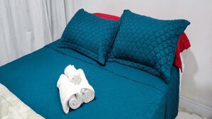 A neatly made bed with teal bedding and a white floral throw, accompanied by rolled white towels. - Moderno Apartamento Centro de Curitiba (Curitiba)