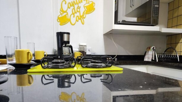 A kitchen with a black countertop, yellow mugs, a coffee maker, and a microwave. - Moderno Apartamento Centro de Curitiba (Curitiba)