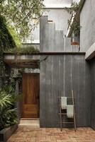Un patio con una puerta de madera, un muro de concreto y una escalera de madera apoyada en él.