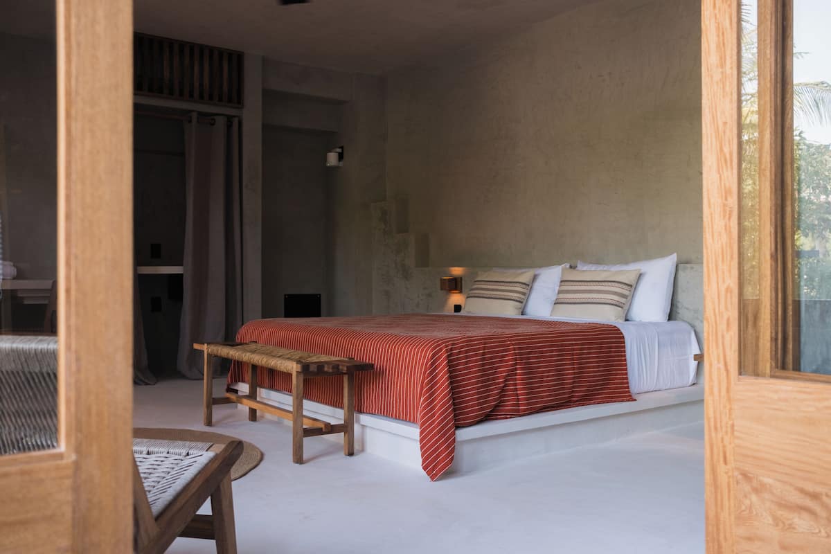 A bedroom with a bed, a wooden bench, and a window.