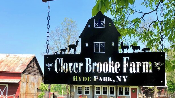 Skilt for Clover Brooke Farm i Hyde Park, New York, med lade og bygning i baggrunden.
