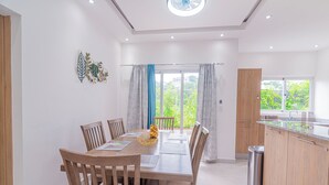 Una cocina moderna con armarios de madera, un lavamanos de acero inoxidable y una zona de comedor con una mesa y sillas de madera.