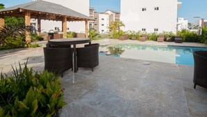 Un área de piscina con mobiliario de mimbre y una zona de estar cubierta.