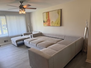 En moderne stue med en hjørnesofa, en loftventilator og en gulvlampe.