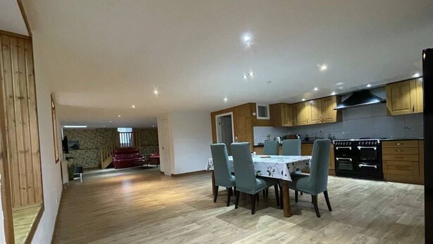 Amplia sala de estar con mesa y sillas de comedor, cocina con armarios de madera y electrodomésticos, y una escalera que conduce a otro nivel.