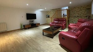 Una sala de estar con una televisión de pantalla plana, un sofá de cuero rojo, una mesa de centro y una escalera.