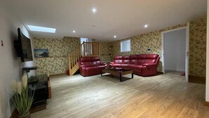 Amplia sala de estar con un sofá de cuero rojo, piso de madera, una escalera y un televisor montado en la pared.
