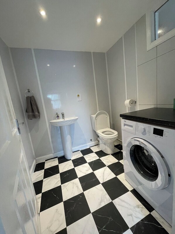 A compact bathroom with a black and white checkered floor, a sink, toilet, and a washing machine.