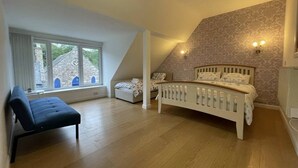 Un dormitorio con techo inclinado, una cama, un banco y una ventana con vista a un edificio de piedra.