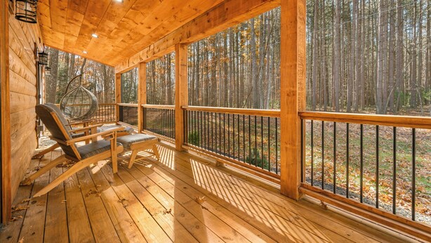 Eine Holzhütte mit Veranda, zwei Liegestühlen und Blick auf einen Wald.
