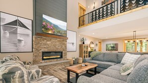Ein großzügiges Wohnzimmer mit Kamin aus Stein, einem großen Sofa und Blick ins Freie vom Balkon aus.