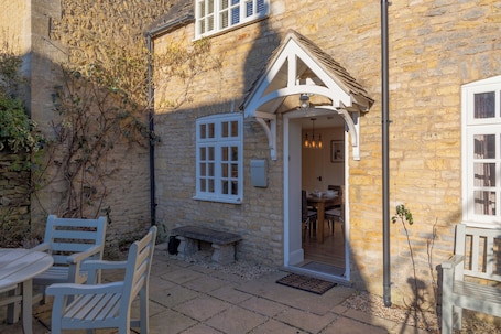 A stone building with a white door and a small porch area with a bench and chairs.
