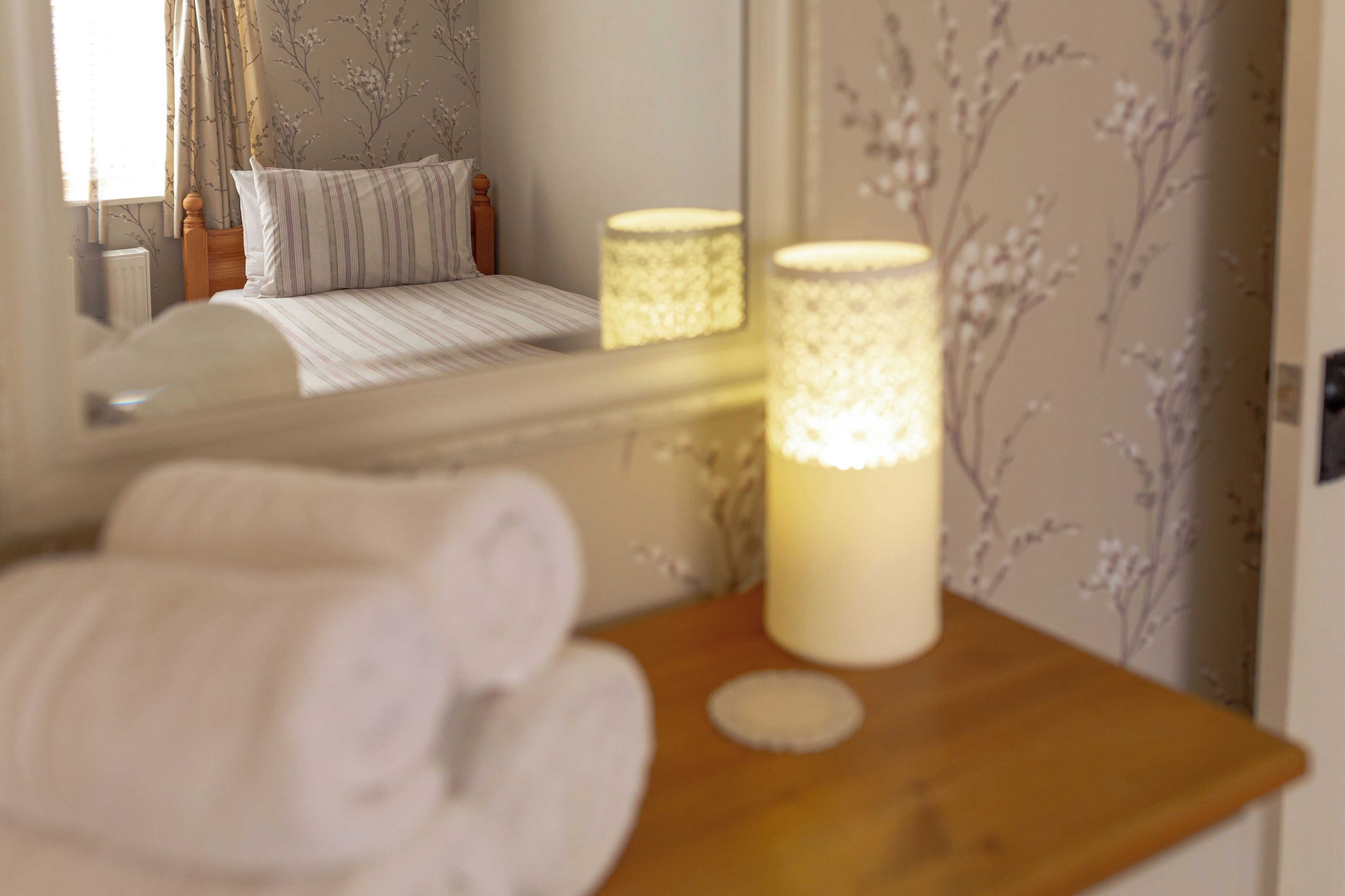 A neatly made bed with striped bedding, a wooden headboard, and a bedside table with rolled towels and a lit candle.