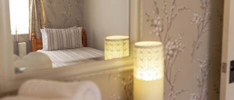 A neatly made bed with striped bedding, a wooden headboard, and a bedside table with rolled towels and a lit candle.