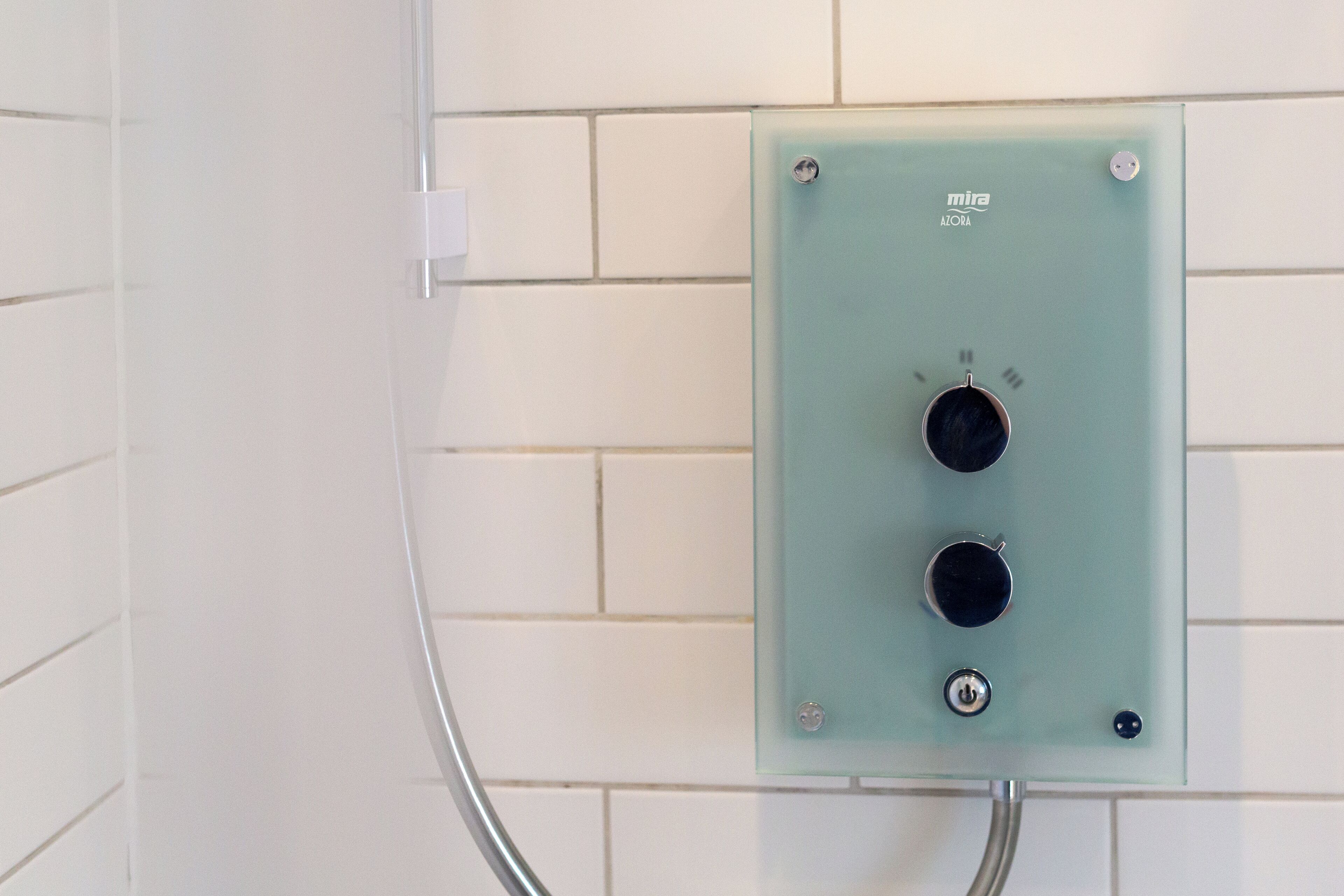 A bathroom with a light green electrical panel mounted on a white tiled wall.