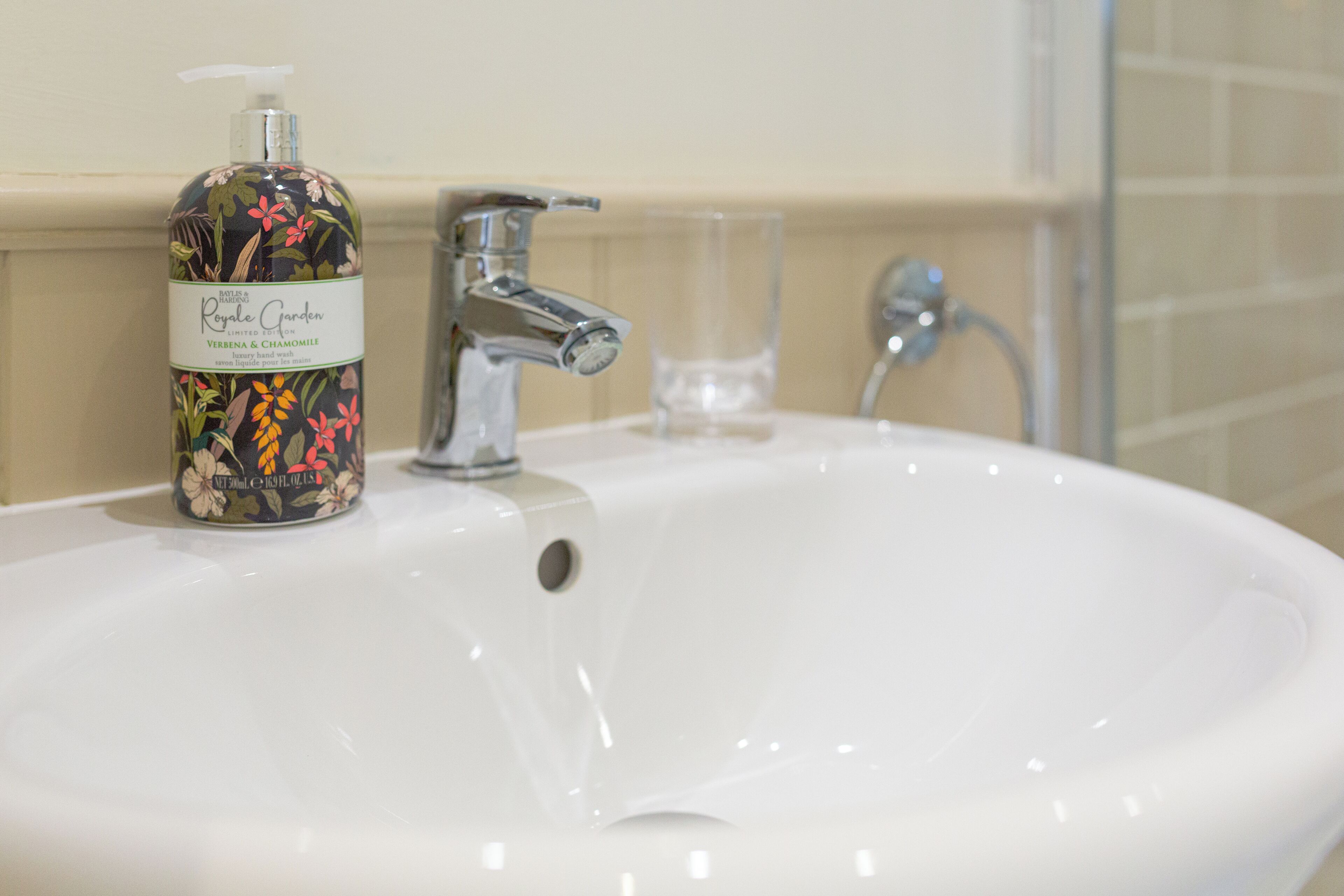 A bathroom sink with a floral soap dispenser, a faucet, and a glass.