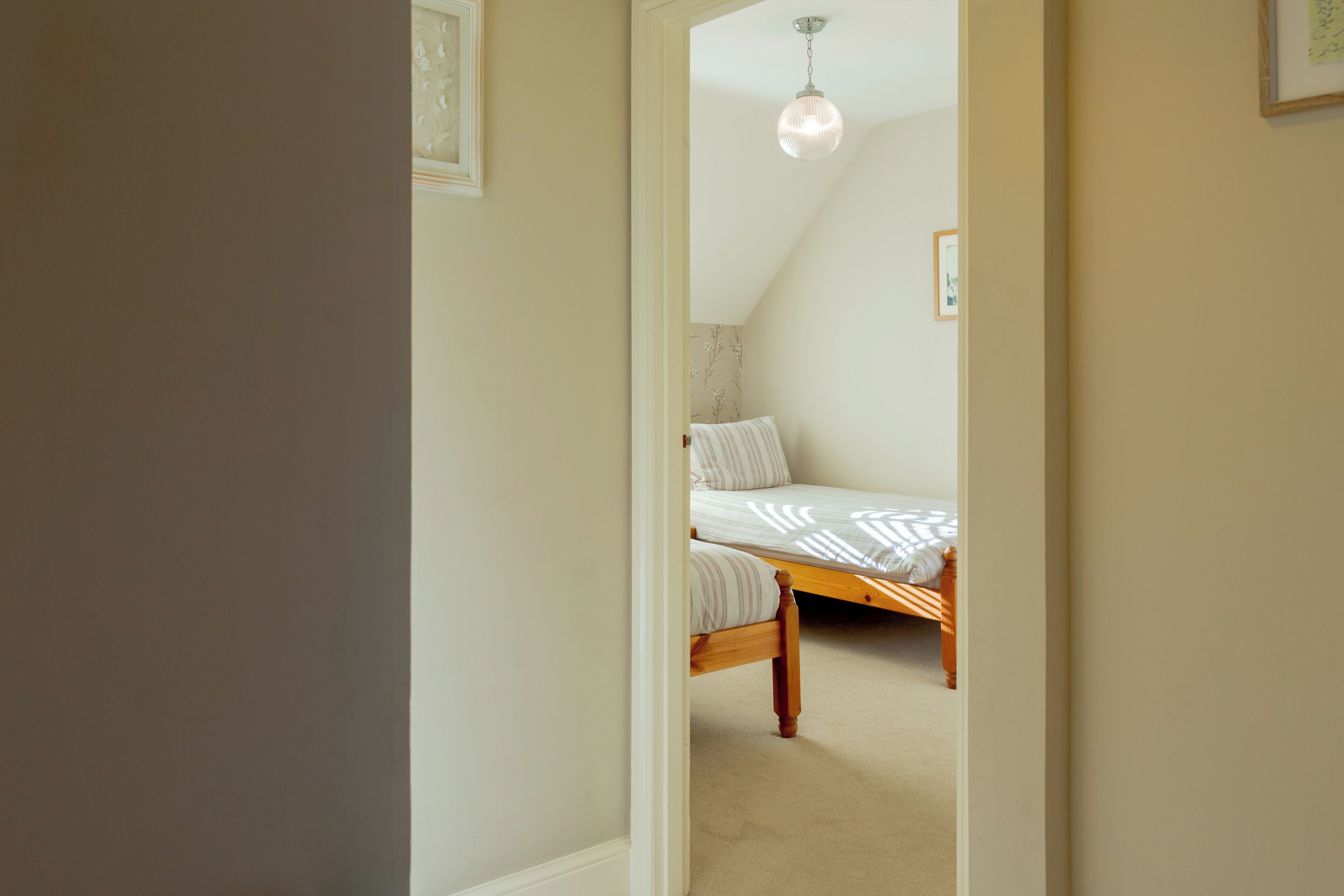 Un dormitorio con una cama individual, una lámpara colgante y un cuadro en la pared.