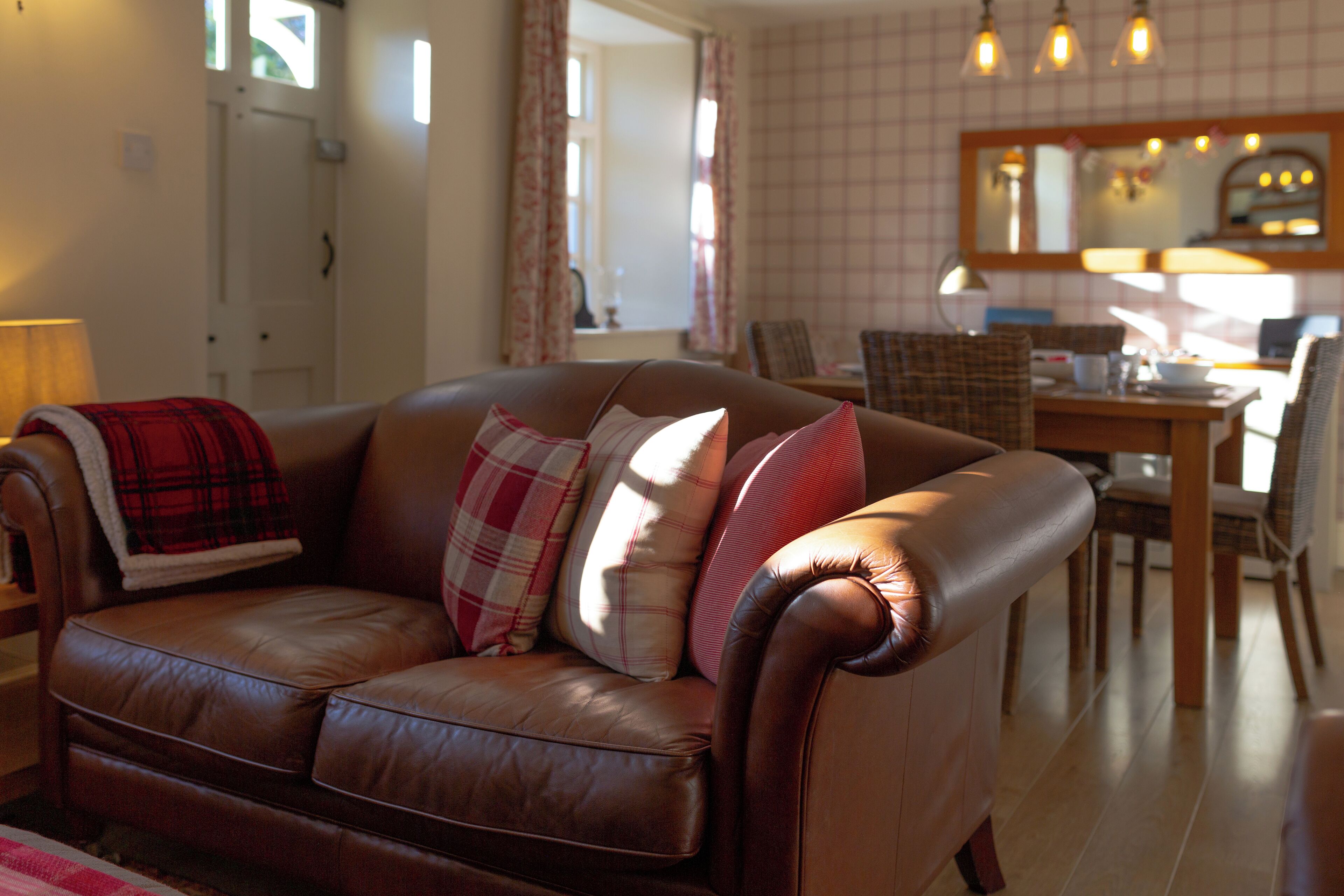 A brown leather sofa with plaid cushions, a wooden dining table, and a mirror above it.