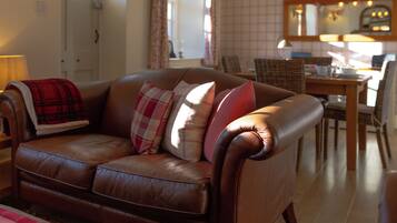 A brown leather sofa with plaid cushions, a wooden dining table, and a mirror above it.