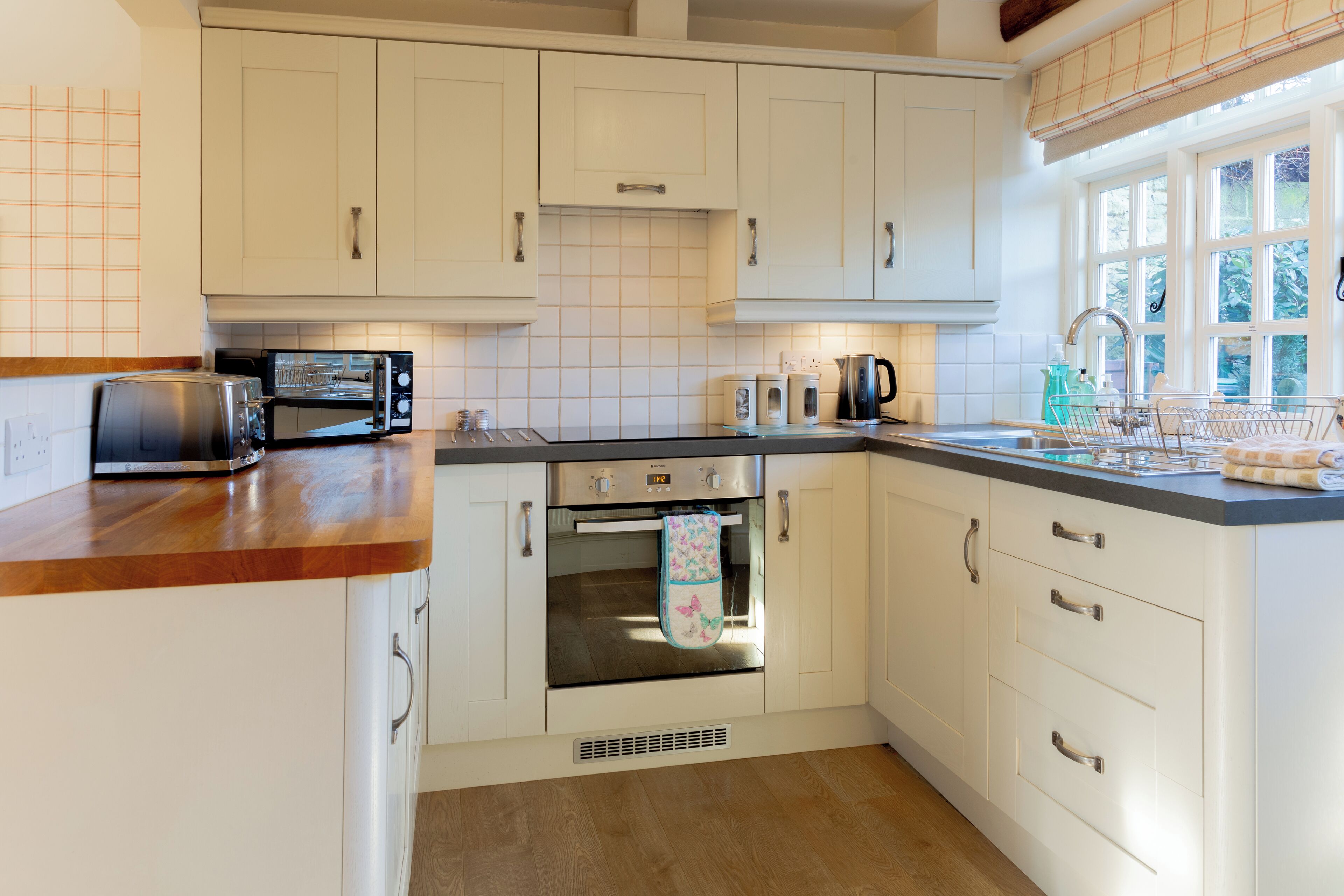 A kitchen with white cabinets, a toaster, a kettle, and a window with a view of greenery.