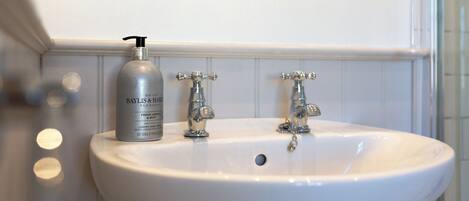 A bathroom sink with a Baylis & Hensley hand soap dispenser, two chrome faucets, and a white tiled wall.