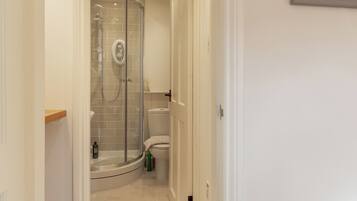 A modern bathroom with a glass-enclosed shower, a toilet, and a small shelf.
