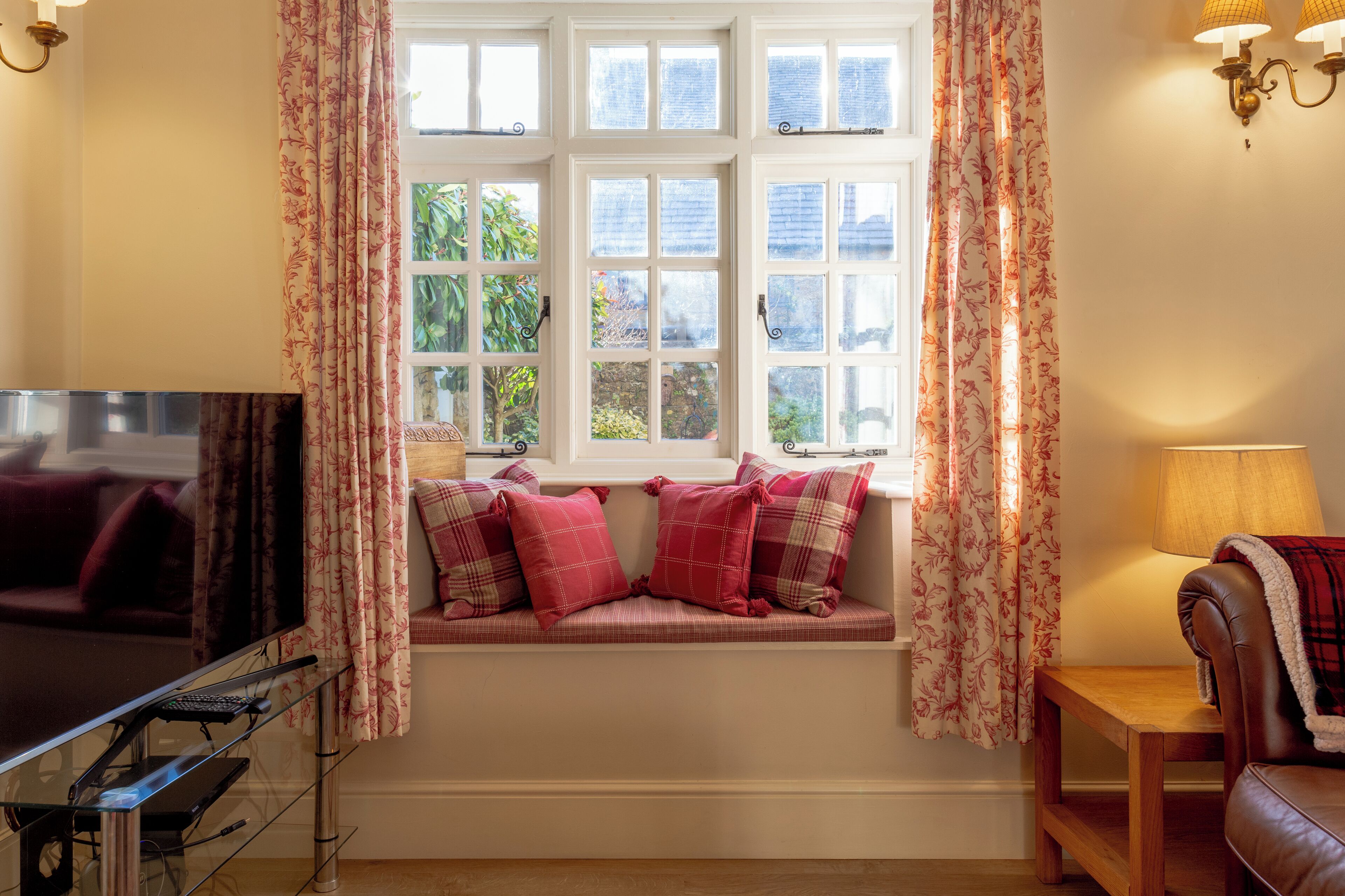 A cozy living room with a large window, a sofa, a TV, and a lamp.