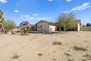 A single-story house with a large backyard, a patio with a table and chairs, and a tree.