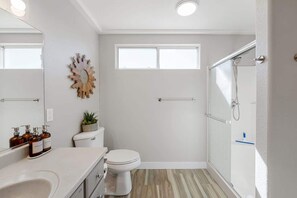 A bathroom with a toilet, a sink, a shower, and a window.