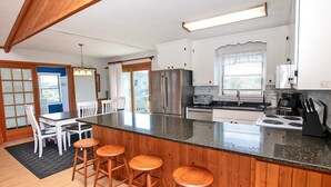 Une cuisine moderne dotée d’un îlot central, de meubles blancs, d’appareils électroménagers en acier inoxydable et de tabourets de bar en bois.