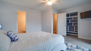 A bedroom with a bed, a ceiling fan, a walk-in closet, and a door leading to another room.