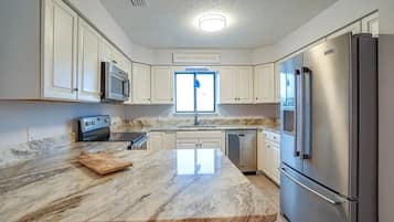 A modern kitchen with white cabinets, a marble countertop, stainless steel appliances, and a window with a view.