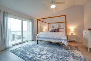 A bedroom with a four-poster bed, a ceiling fan, a large window with curtains, a nightstand with a lamp, and a dresser. - Gulf-View Townhome · 30 Steps to Beach (Port St. Joe)
