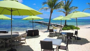 Un restaurante frente al mar con terraza, que incluye mesas y sillas, y sombrillas verdes.