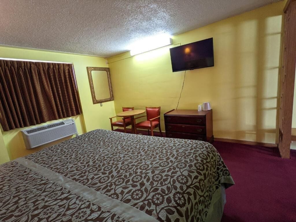 A hotel room with a bed, a desk, a chair, a television, and a window with curtains.