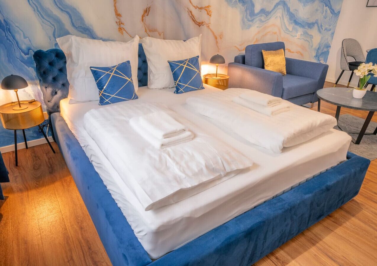 Une chambre moderne avec un grand lit, un canapé bleu recouvert de tissu et une petite table ronde.