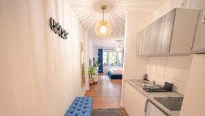 A narrow hallway with a blue bench, a kitchen area with a sink and stove, and a bedroom visible in the background. - Noble Studio | 1 Min to HBF (Mannheim)