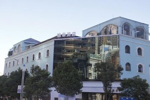 Un hotel con fachada azul claro, varios balcones y una sección de vidrio.