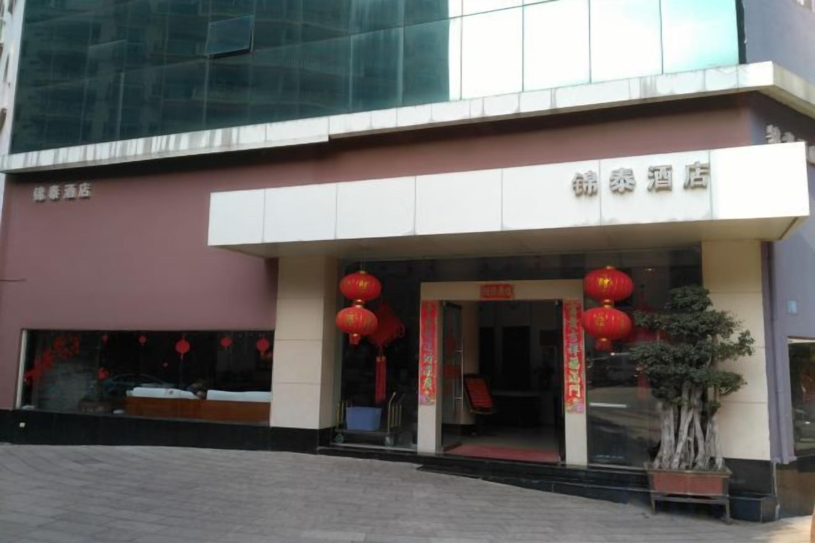 A hotel entrance with a modern facade, a red lantern decoration, and a potted plant.
