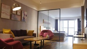 A modern hotel room with a sofa, a dining table, a red chair, a bed with a headboard, a TV, and a large window. - Jin tai Hotel (Gejiu)