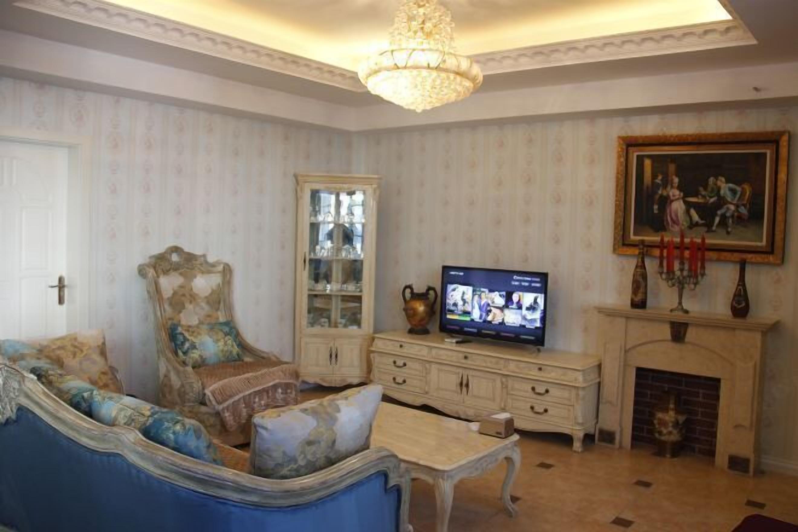 A living room with a sofa, television, cabinet, fireplace, and a chandelier.