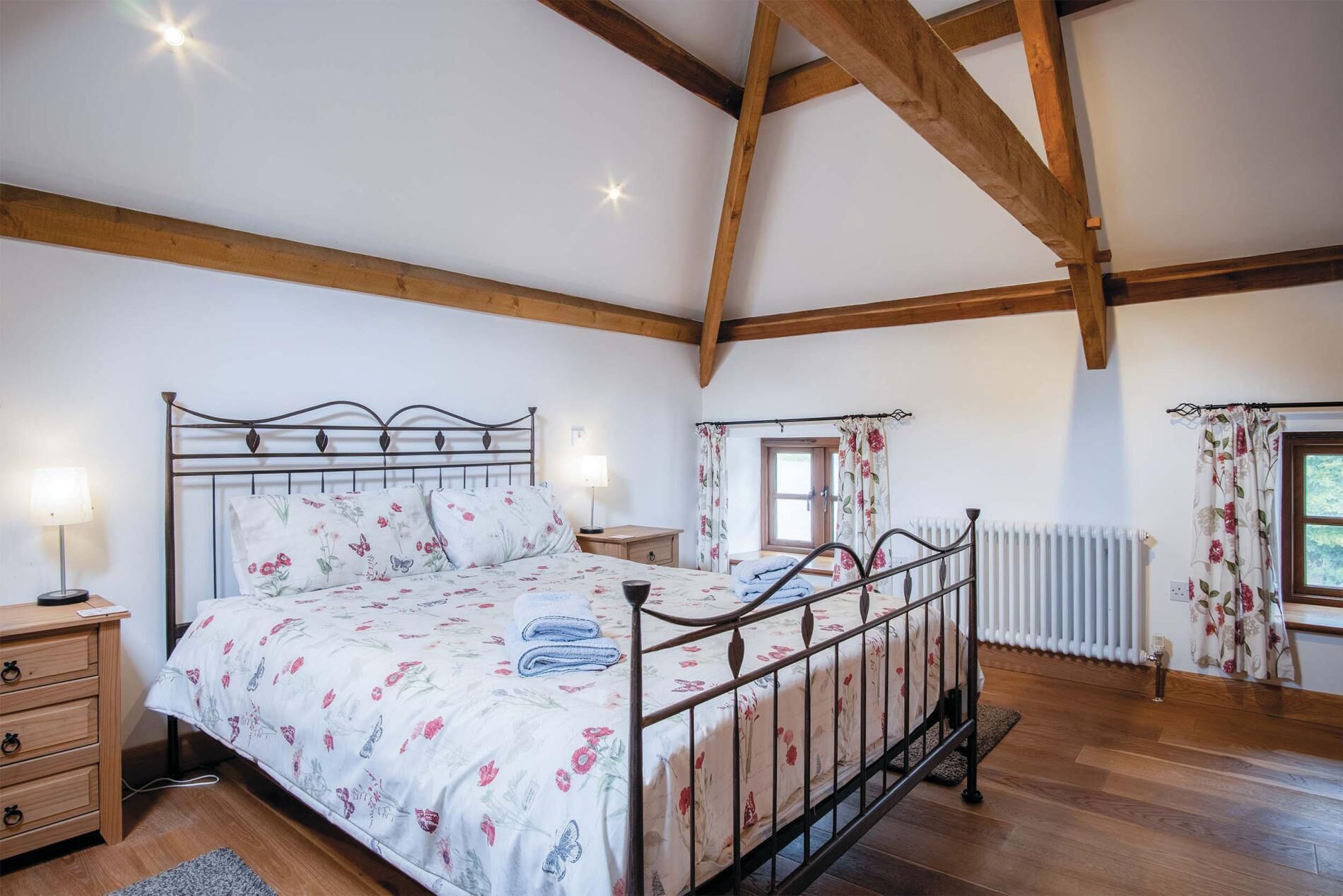 A bedroom with a bed, wooden beams, a radiator, and a window with curtains.