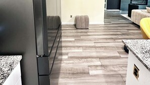 A modern kitchen with a stainless steel refrigerator, wooden flooring, and a grey sofa in the living area. - Spacious 4 bedroom house with fitness room and WiFi in charming Glenn Heights. (Glenn Heights)
