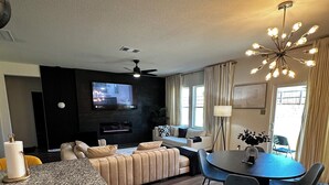 A modern living room with a sofa, TV, and dining area. - Spacious 4 bedroom house with fitness room and WiFi in charming Glenn Heights. (Glenn Heights)