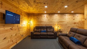A wooden-paneled room with a leather sofa, a television mounted on the wall, and a small table with a lamp. - Moonlight Ridge Lodge - Hocking Hills (Logan)
